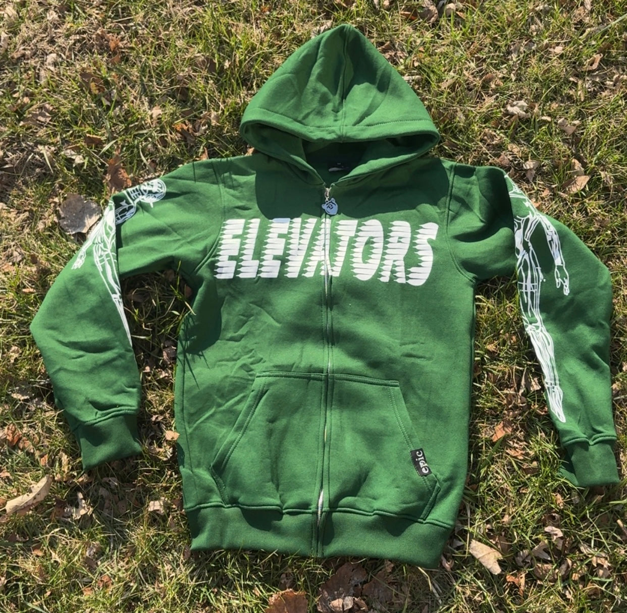 Elevators Hoodie displayed on grass, featuring a vibrant green color and unique graphic design for a motivational lifestyle.